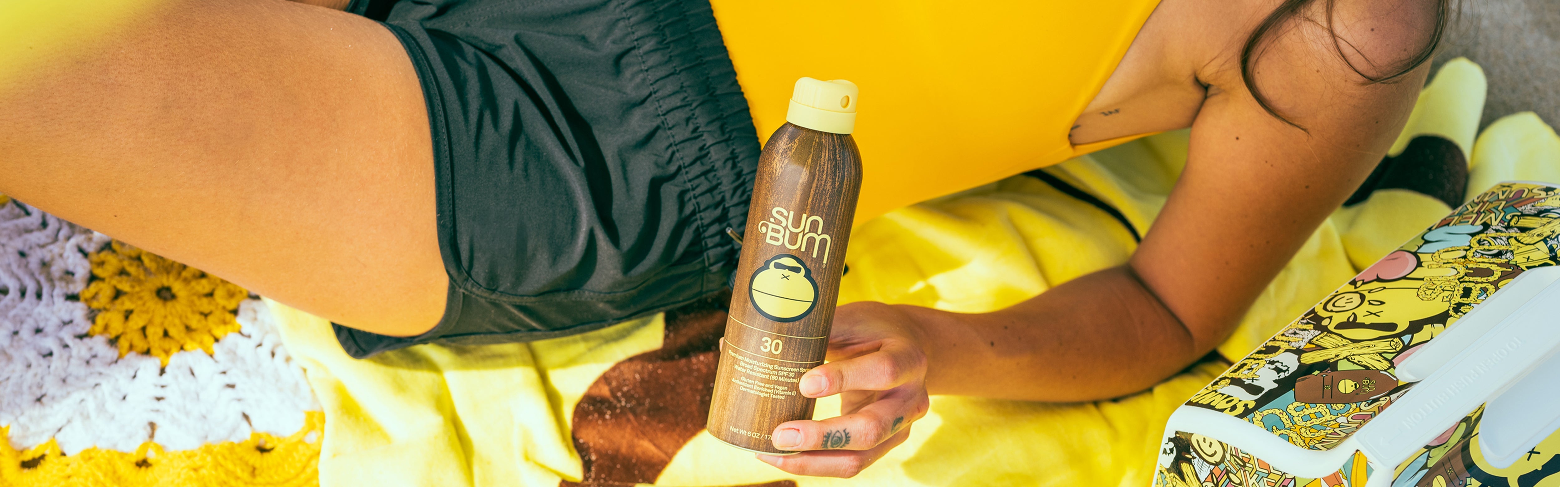 Close-up of Sun Bum SPF 30 spray sunscreen on a beach towel, part of the Regulated Shipping Collection – Sun Bum.