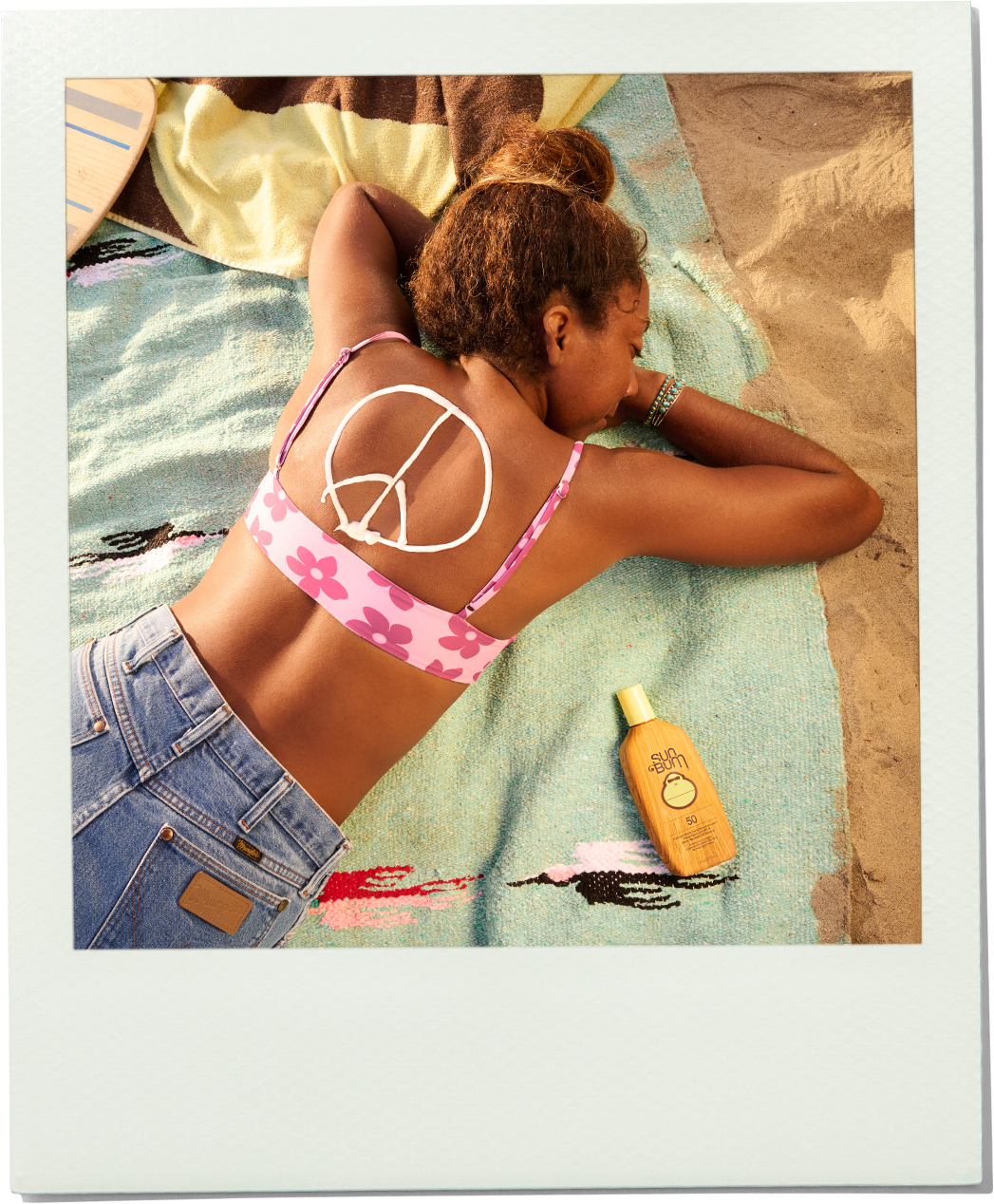 Woman in a bikini lying on a towel with a sun screen bottle next to her at the beach.