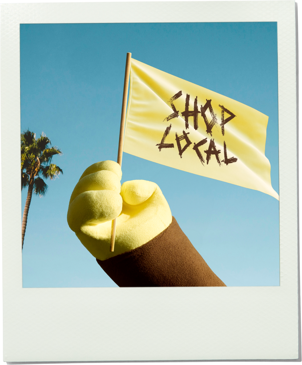 Hand holding a yellow flag with 'Shop Local' text against a blue sky with palm trees.