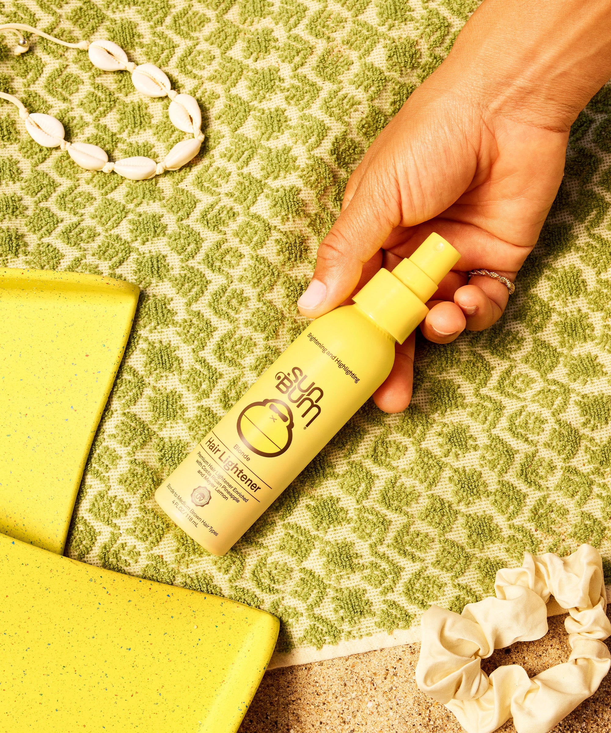 Hand holding Blonde Hair Lightener spray with tropical background by Sun Bum