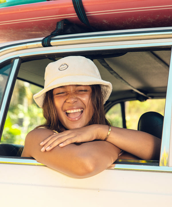 Woman wearing a Plush Bucket Hat, smiling and leaning out of a car window, enjoying a sunny day. Sun Bum,