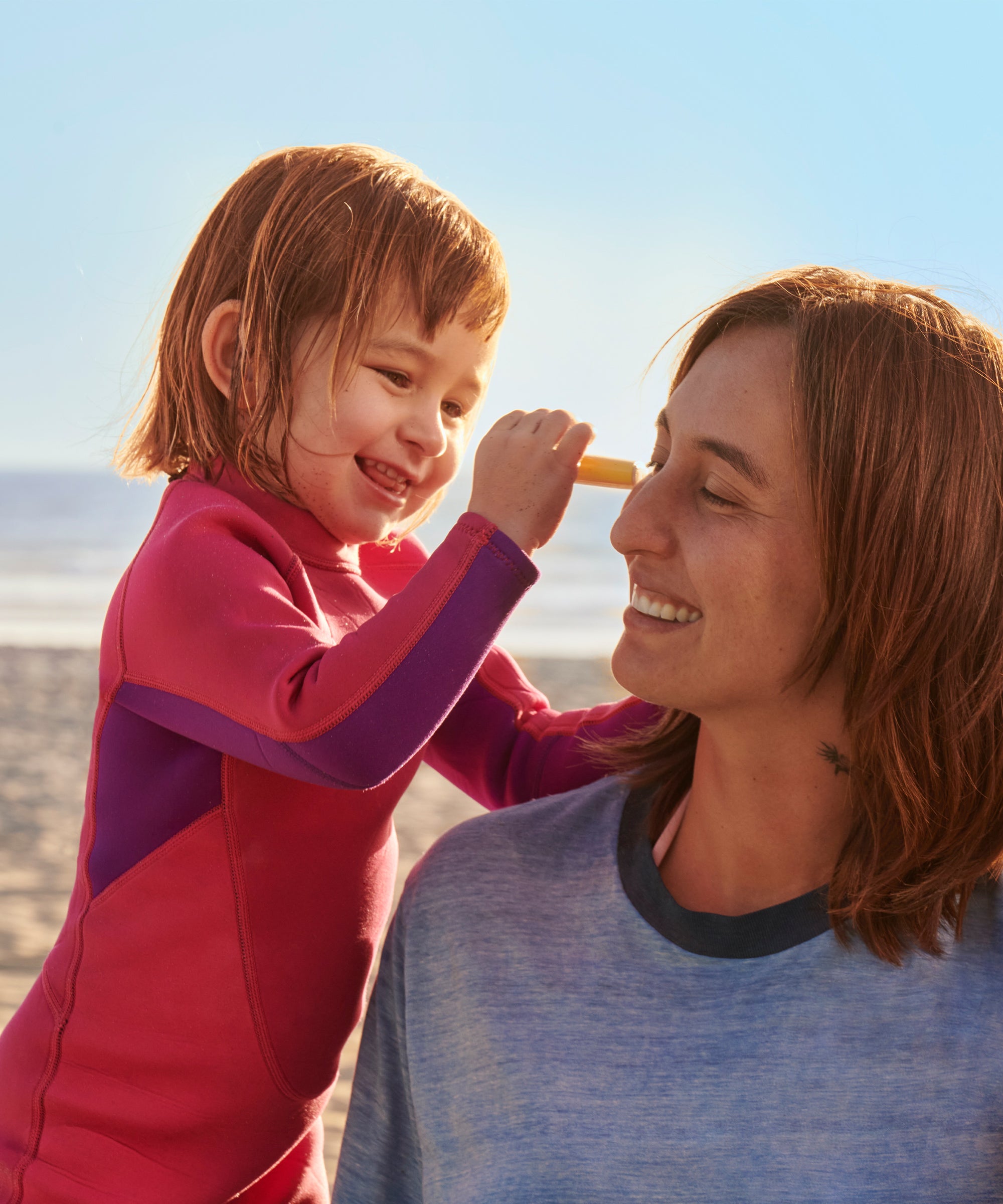 Child applying Baby Bum SPF 50 Sunscreen Face Stick to a mother's nose at the beach, Baby Bum.