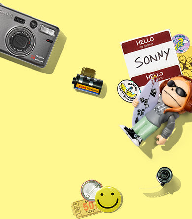 Camera, film roll, and figurine with 'Hello Sonny' sign on a yellow background