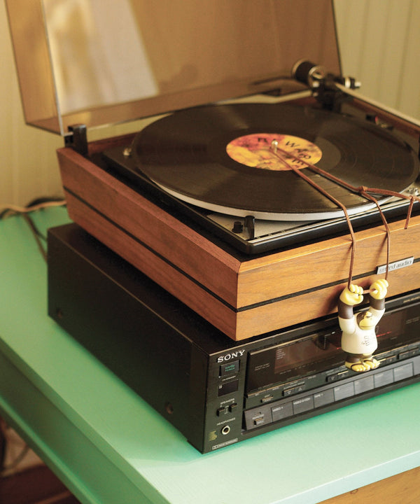 Close-up of 'Lucky Bum' figure hanging from a retro turntable setup, enjoying some good vinyl vibes. Sun Bum.