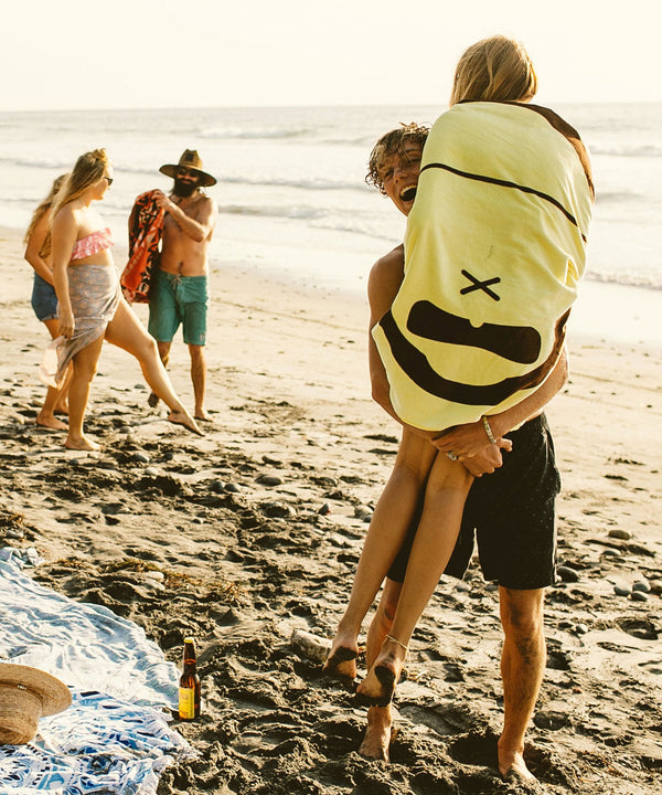 Beachgoers carrying 'Sonny' Beach Towel, enjoying a sunny day, Sun Bum.