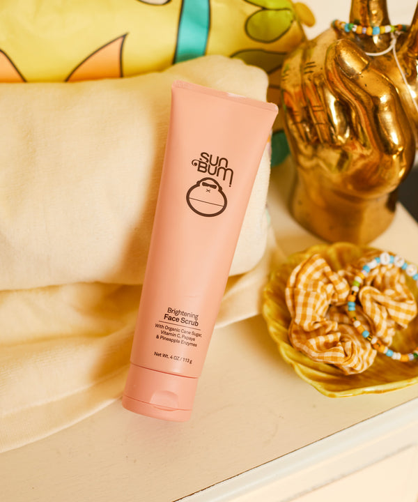 Brightening Face Scrub tube on a cozy display. Made with Papaya & Pineapple Enzymes and Organic Cane Sugar for smooth, exfoliated skin. Sun Bum.