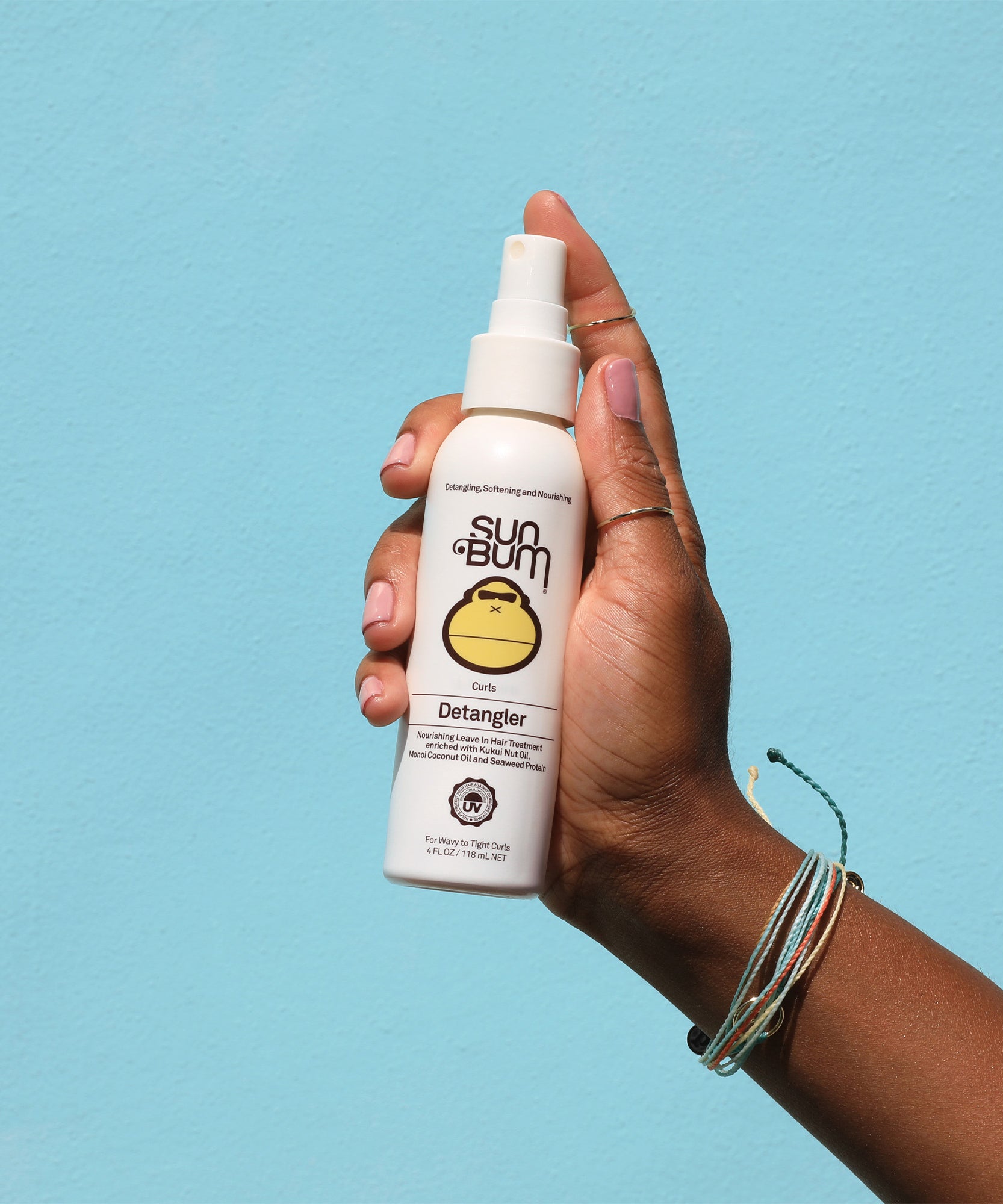 Hand holding Sun Bum Curls Detangler spray made with Kukui Nut and Monoi Coconut Oil for curly hair conditioning.