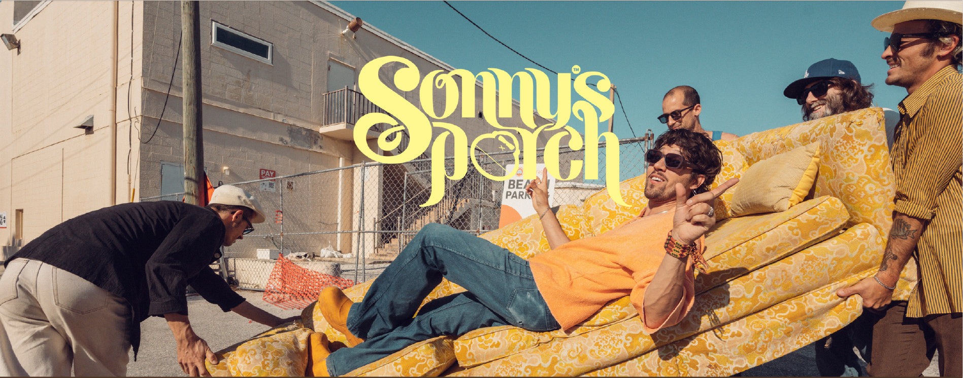 Album cover art for 'Sonny's Porch' featuring a group of people carrying a yellow patterned couch in an outdoor industrial setting under a clear blue sky, with the stylized yellow title text at the top.