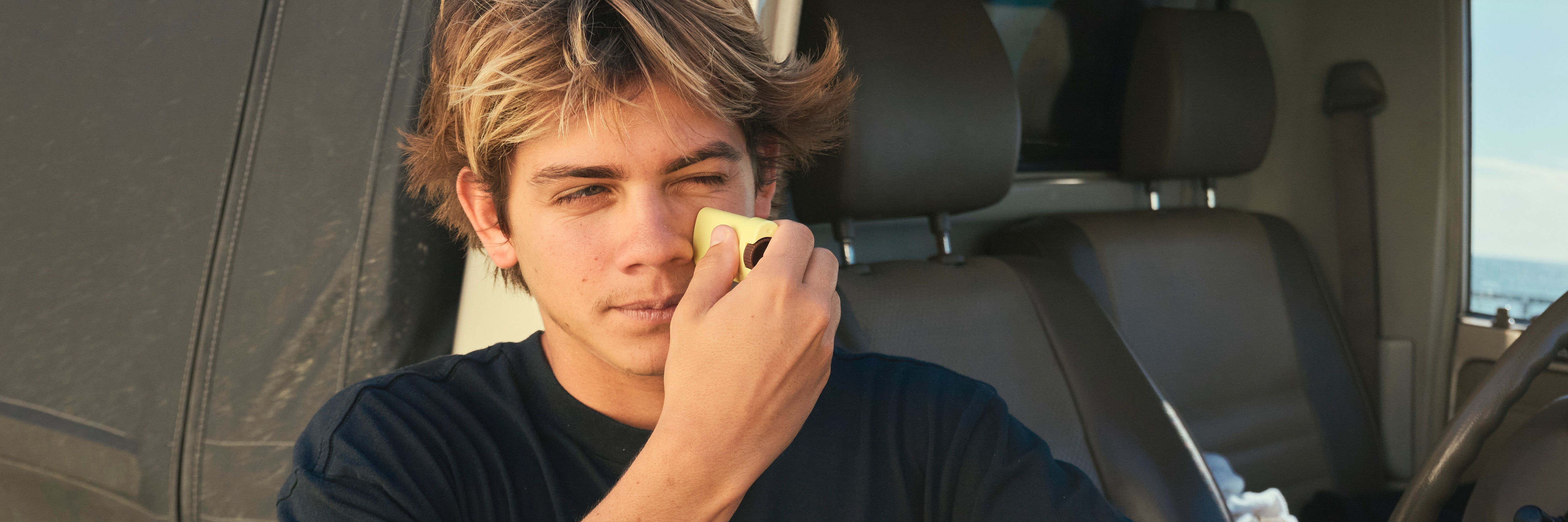 Person sitting in a car holding a yellow object to their ear
