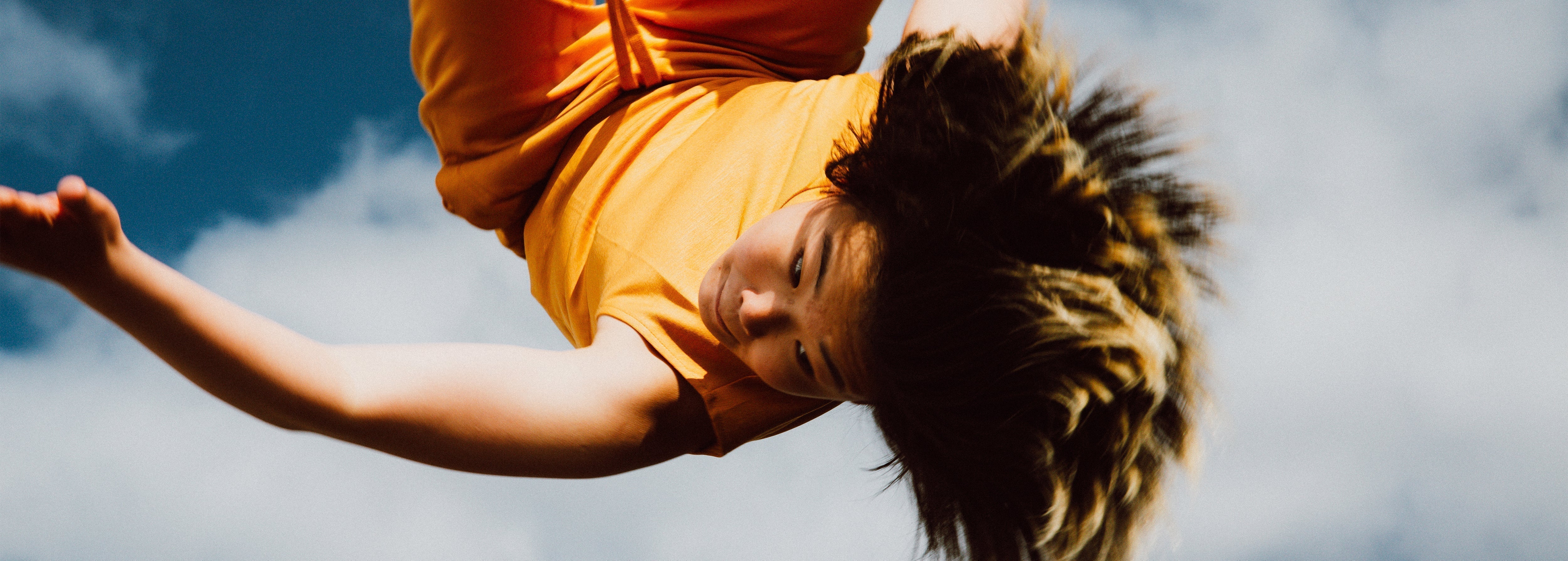 Person in an orange shirt upside down against a blue sky