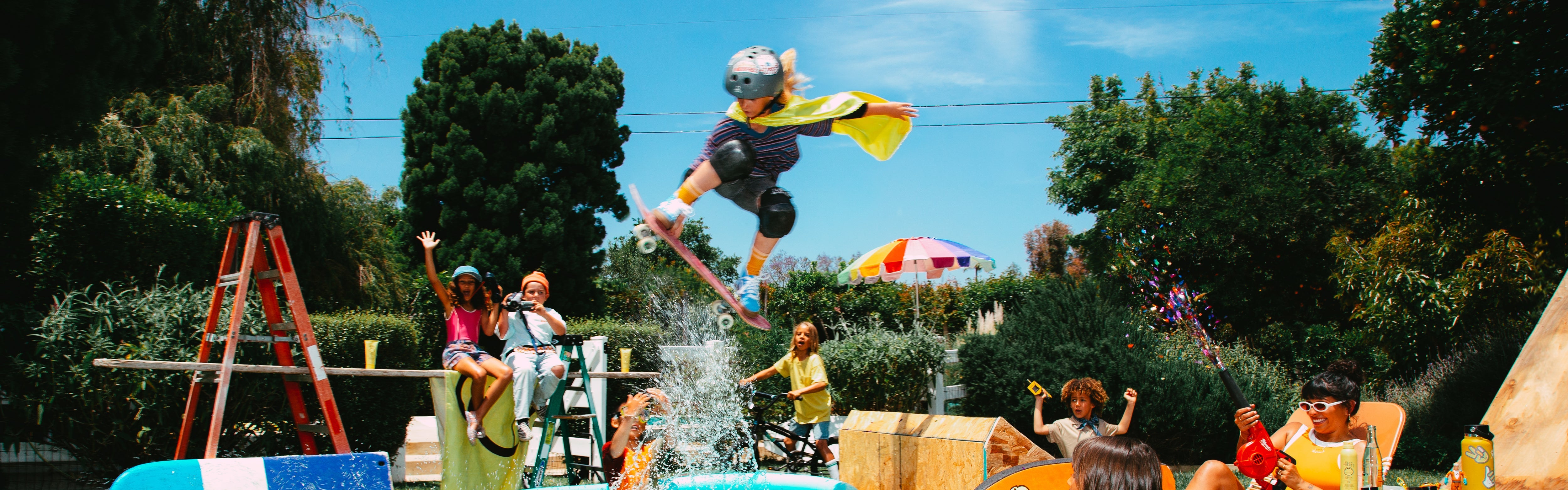 Kids playing in a backyard, one jumping over a kiddie pool on a skateboard, featuring the SB Kids Sunscreen Collection – Sun Bum.