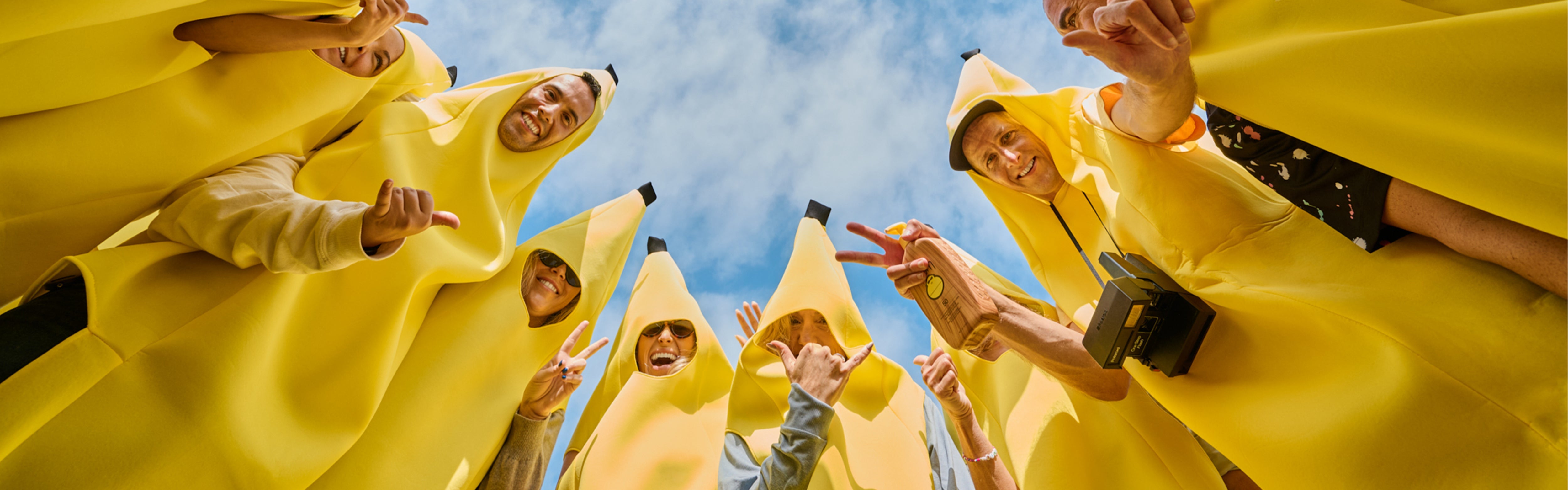 Group of friends in banana costumes throwing peace signs and holding sunscreen from the SB Original Sunscreen Collection – Sun Bum.