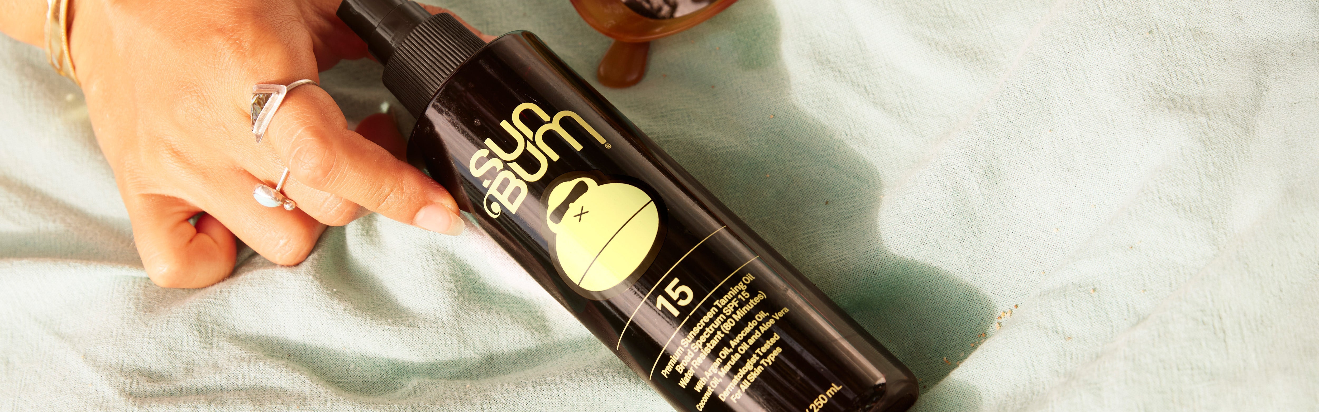 Sun Bum SPF 15 Tanning Oil on a beach towel with papaya and sunglasses, from the SB Tanning Oils and Lotions Collection – Sun Bum.