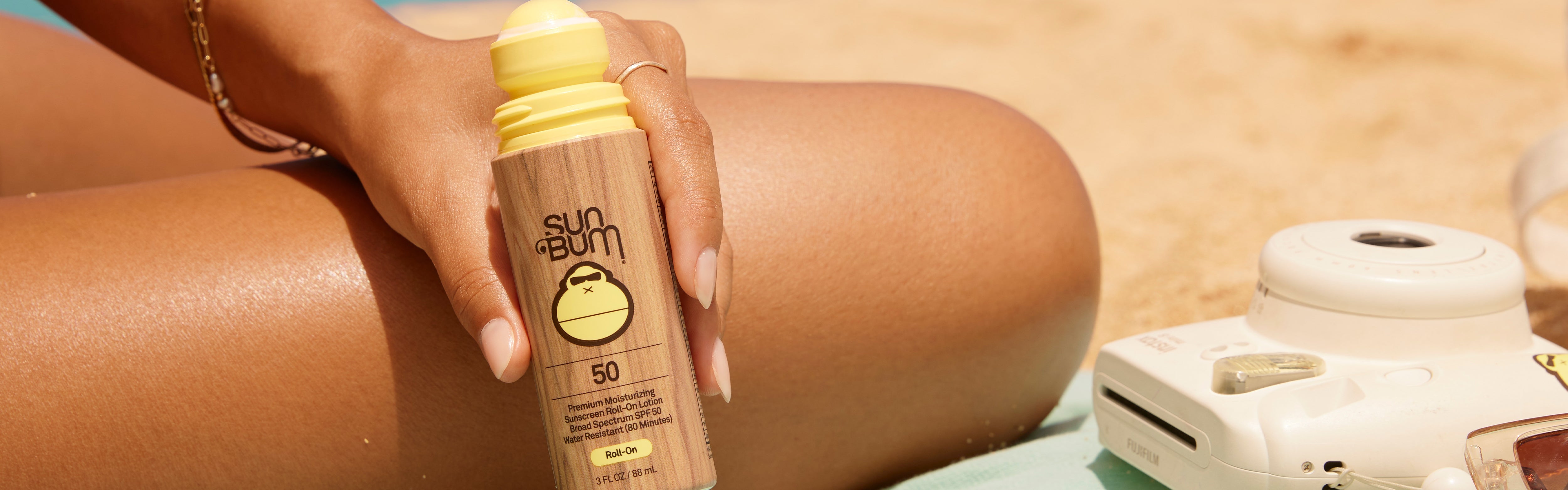 Hand holding Sun Bum SPF 50 Roll-On Sunscreen at the beach, part of the Roll Ons Collection – Sun Bum.