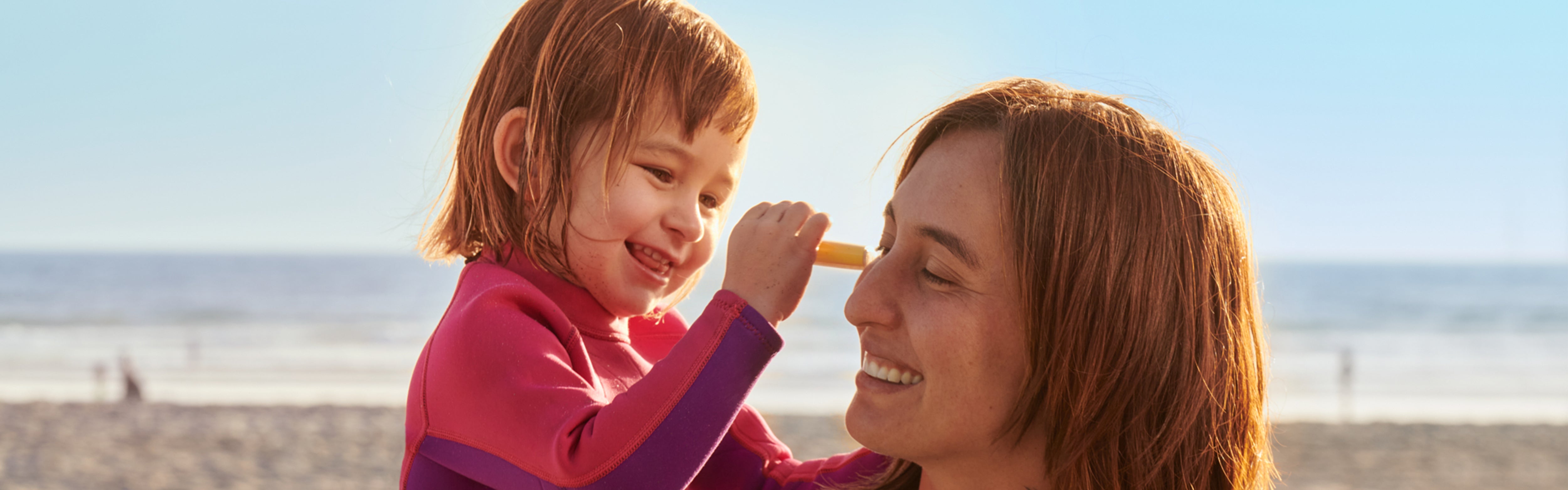 Smiling child applies sunscreen stick on parent’s nose at the beach – Sunscreen Sticks Collection - Sun Bum.