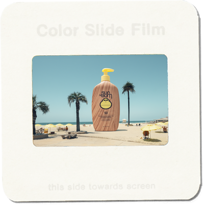 Suntan lotion bottle on a beach scene with palm trees and blue sky.
