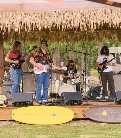 Band performing on a stage with a thatched roof in a outdoor setting