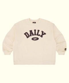 An off-white crewneck sweatshirt featuring a dark brown graphic on the chest that reads 'DAILY SPF' with 'SPF' inside an oval. A small brand tag is visible on the left sleeve cuff, and the inner collar shows the brand name 'DAILY'.