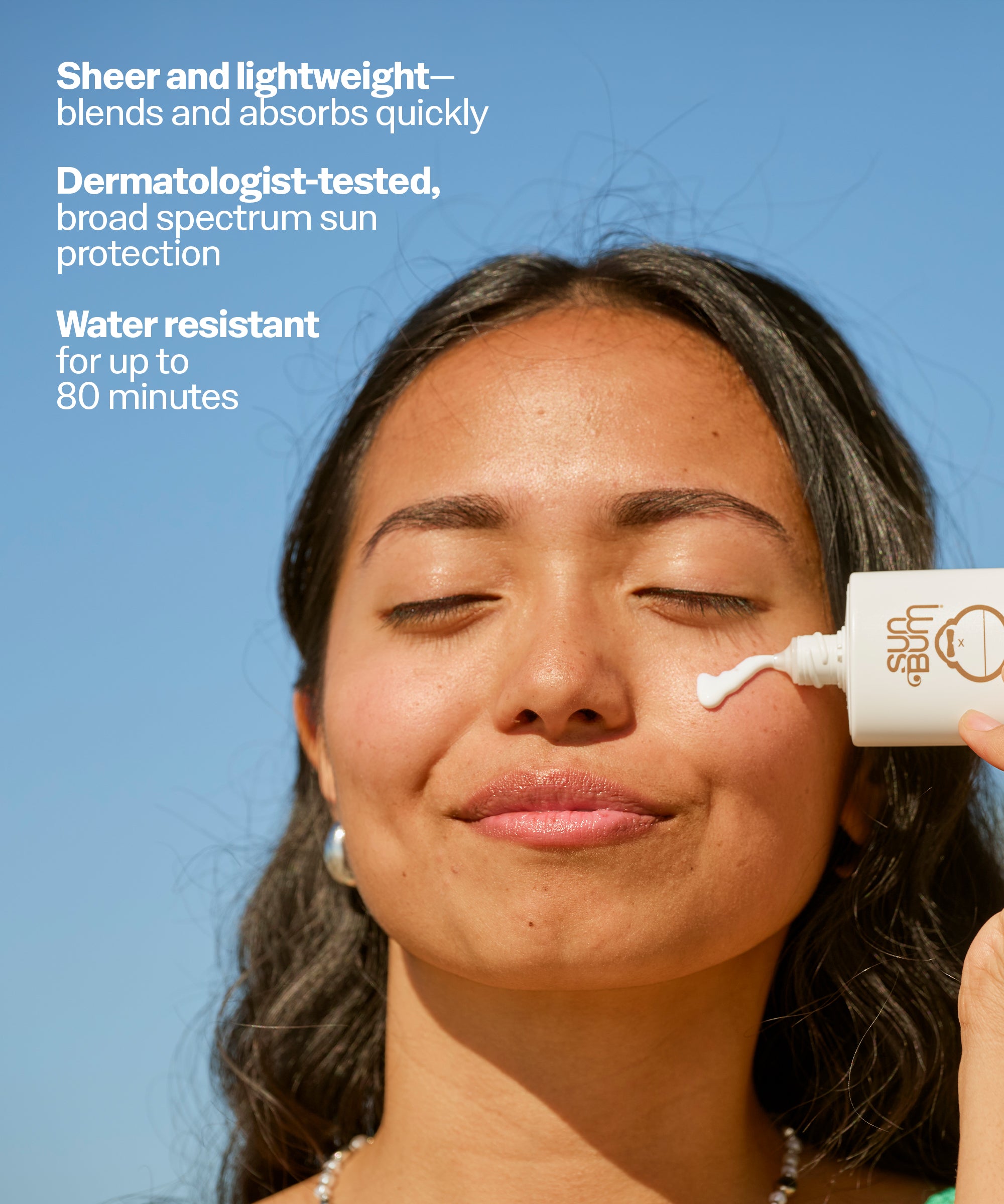 Woman applying sunscreen to her face with a clear blue sky background