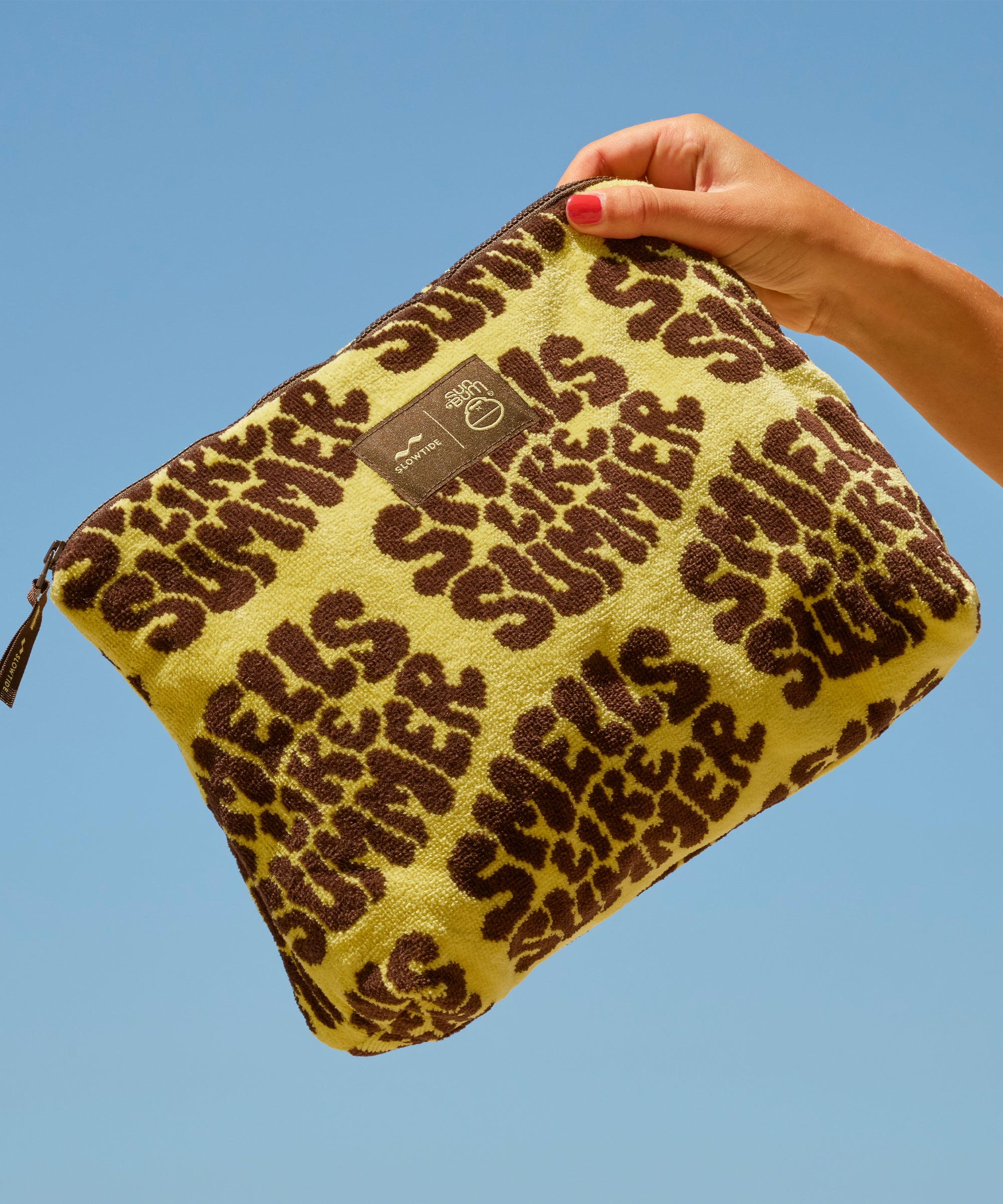 Yellow pouch with brown leopard print text held against a blue sky