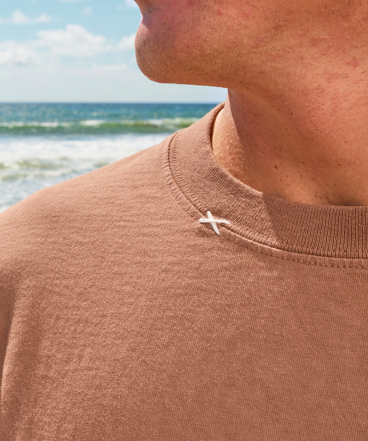 Original Tee (Brown) worn by a person with ocean waves in the background