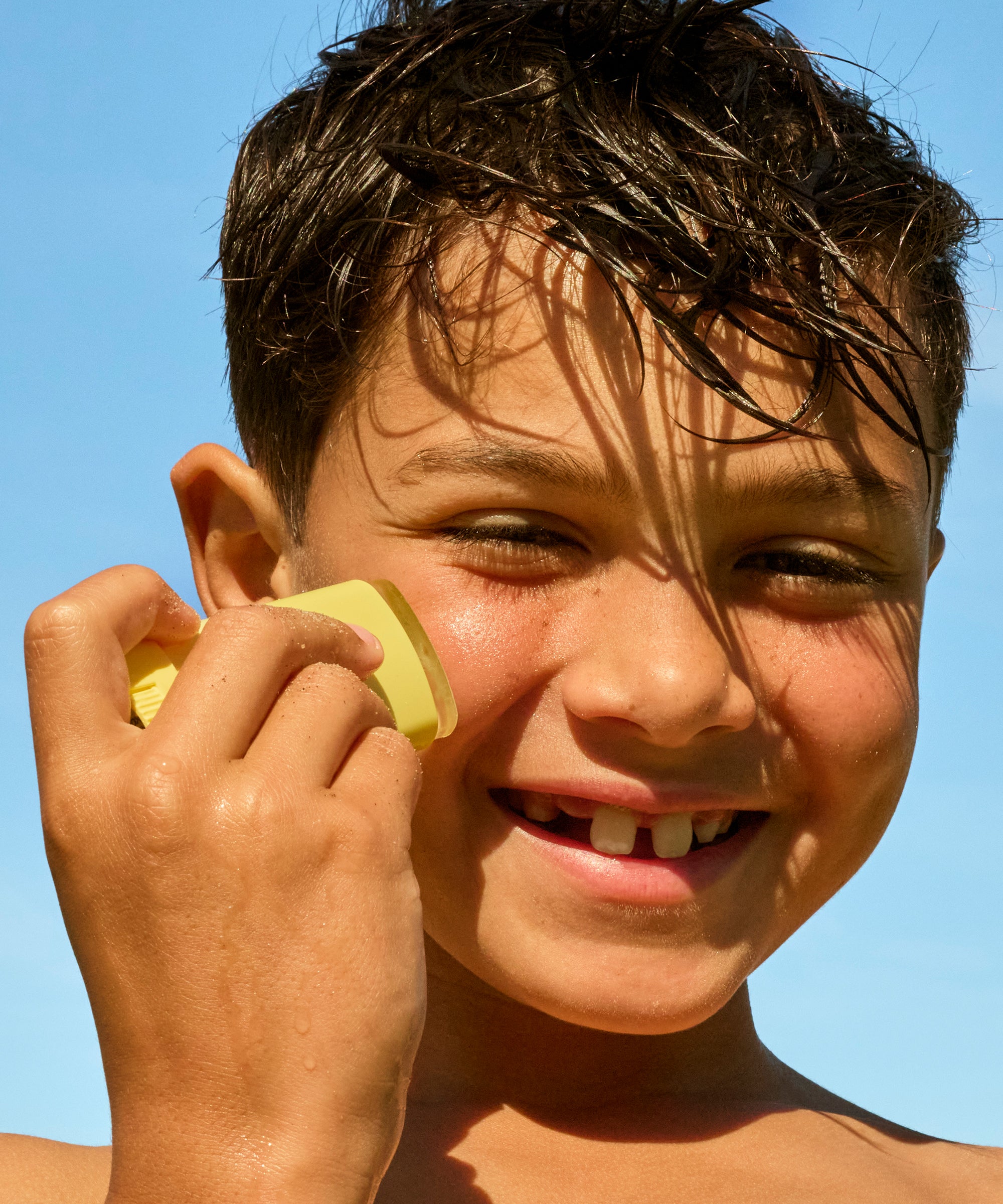 Child holding a yellow object to their ear with a clear blue sky background