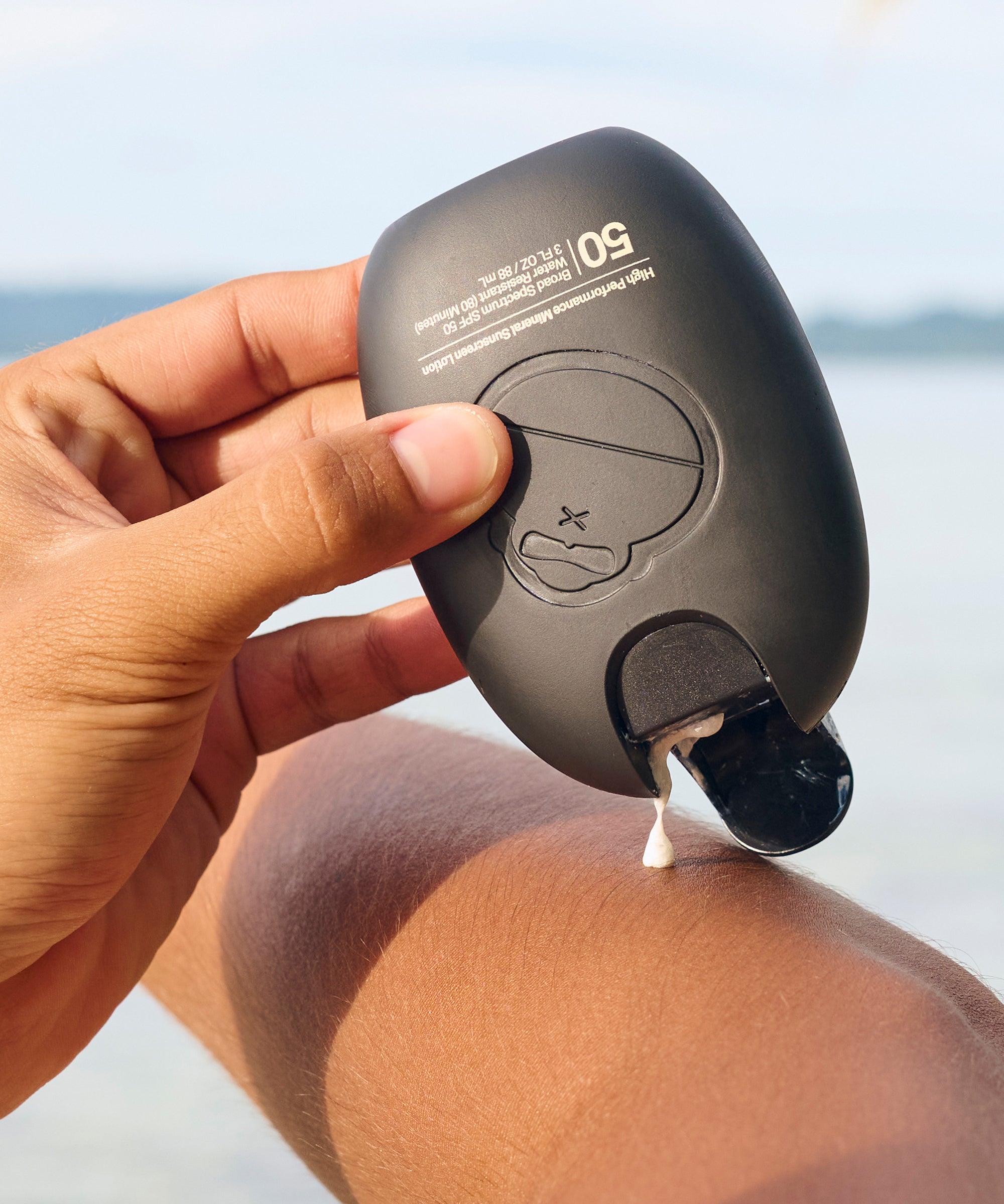 Hand holding Sun Bum Signature Mineral Lotion, Face Stick & Lip Balm Bundle applying lotion to leg outdoors by water