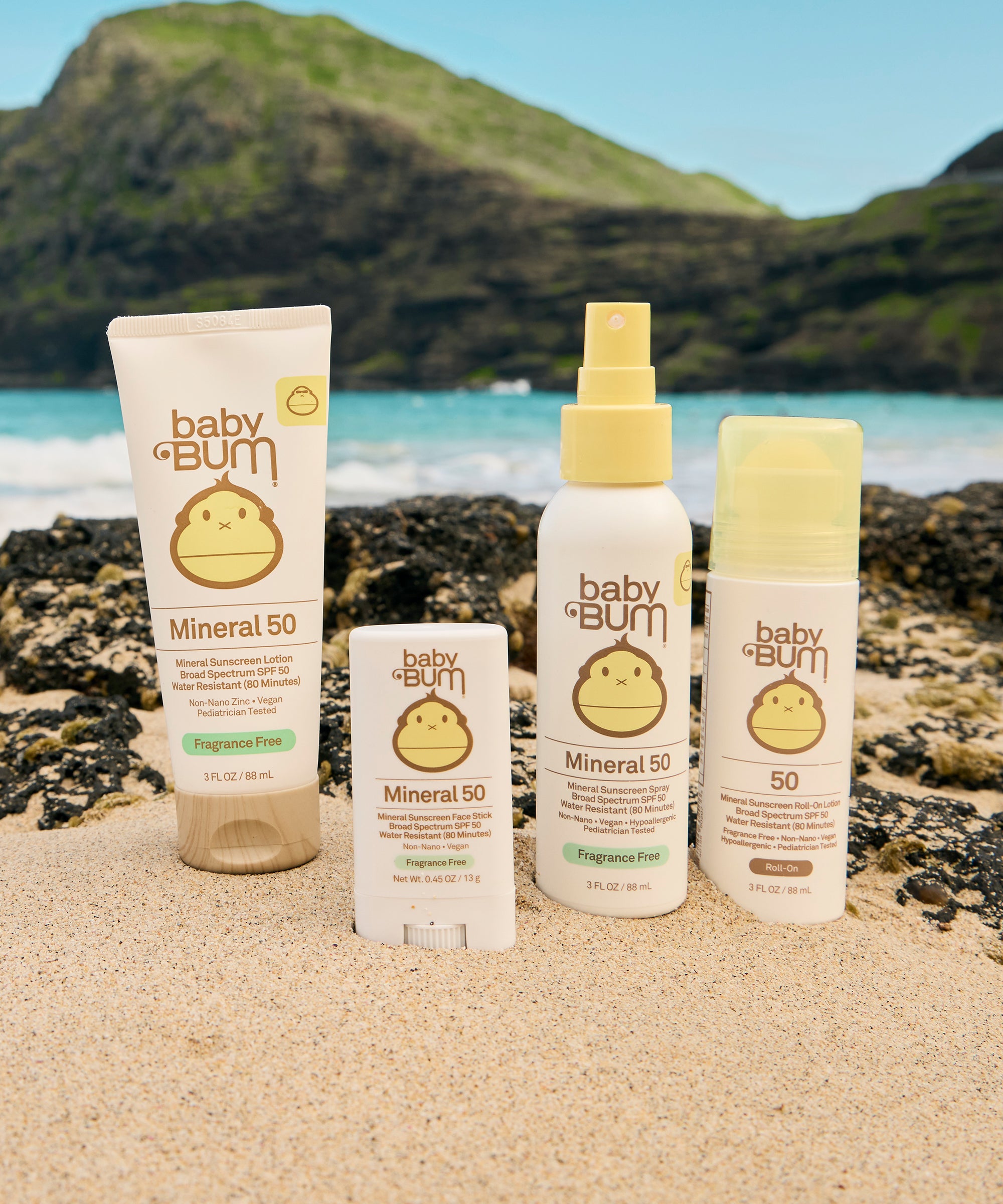 Baby Bum mineral 50 sunscreens on a beach with ocean and mountains in the background