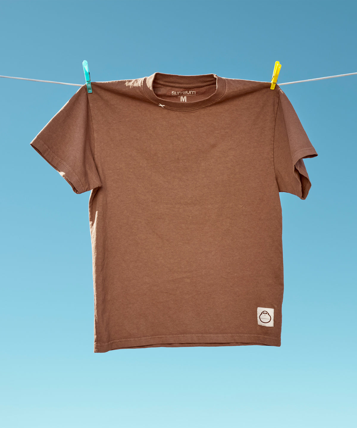 Original Tee (Brown) hanging from a clothesline against a clear blue sky