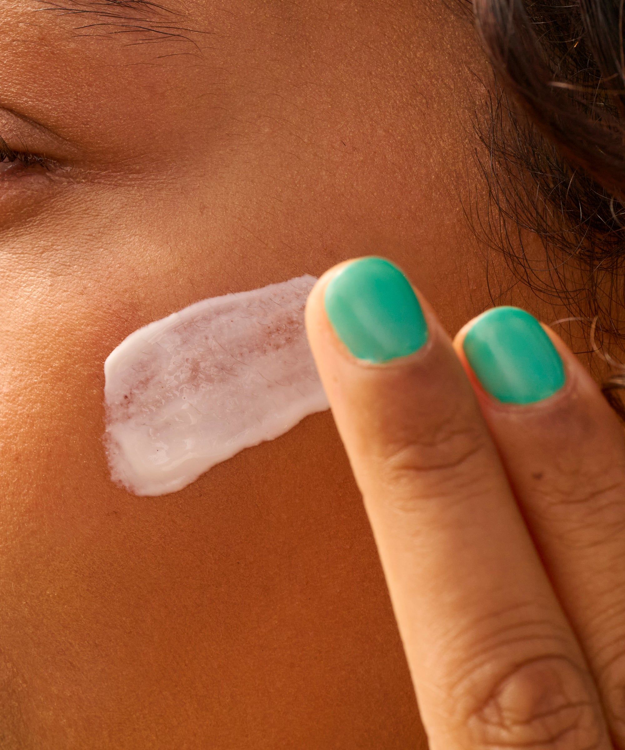 Person applying sunscreen cream to their cheek with a finger.