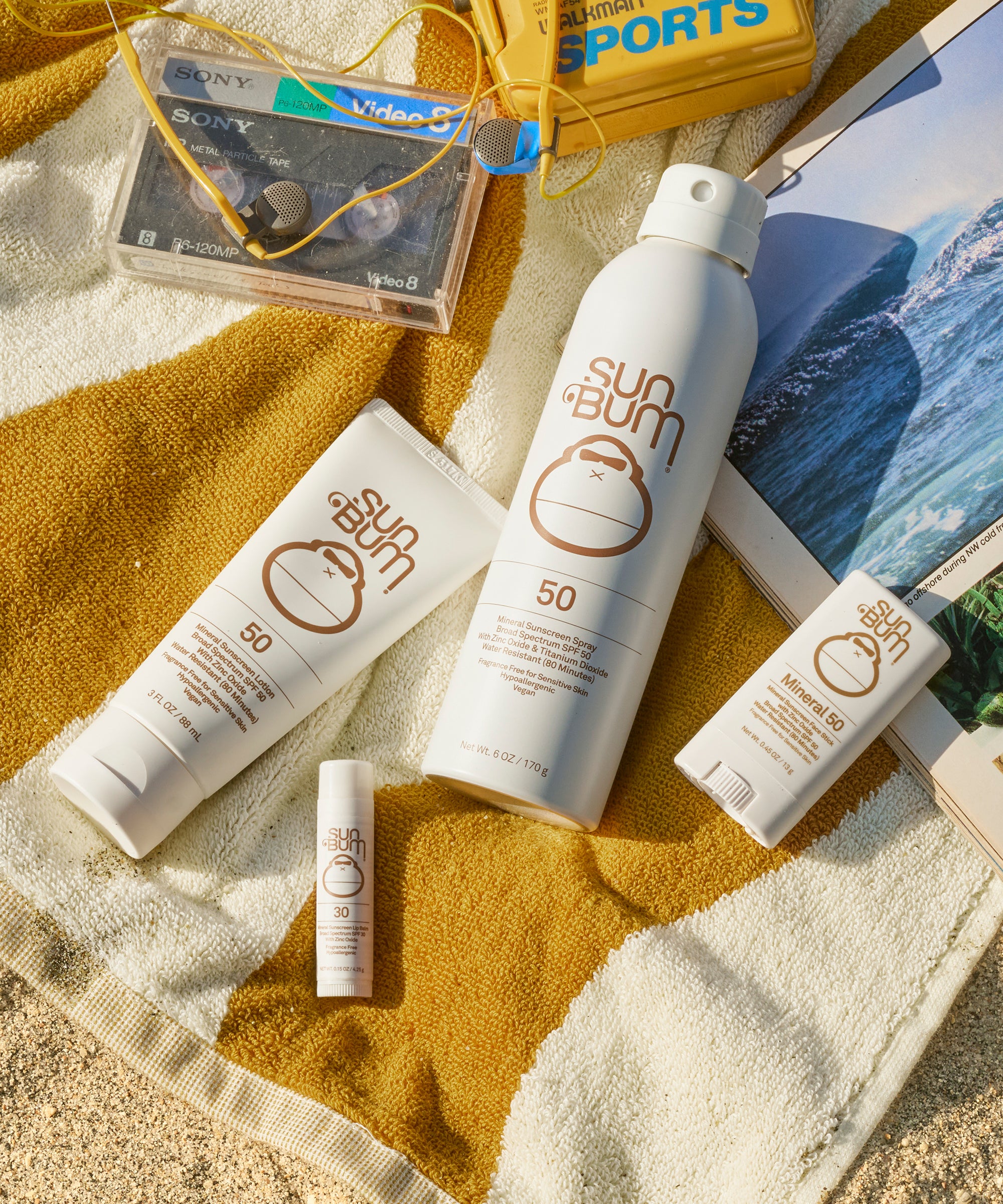 Sun Bum sunscreen products on a towel with a magazine and cassette tape in the background