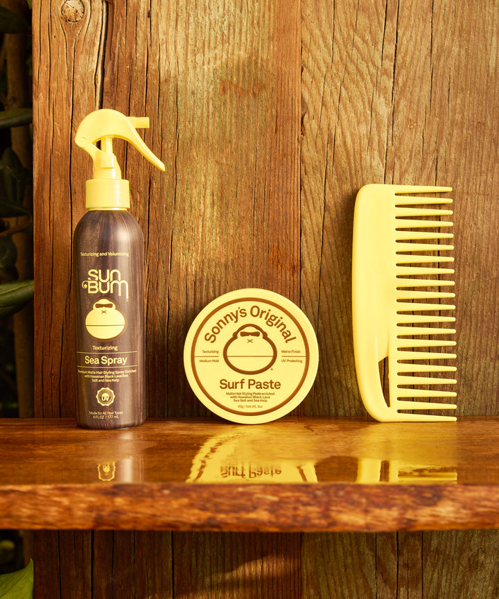Texturizing Surf Paste displayed alongside Sun Bum sea spray and a yellow styling comb on wooden shelf, creating a complete hair styling set for effortless beach-inspired looks - by Sun Bum