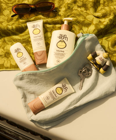 Sun Bum sunscreen products on a towel with sunglasses and keys.