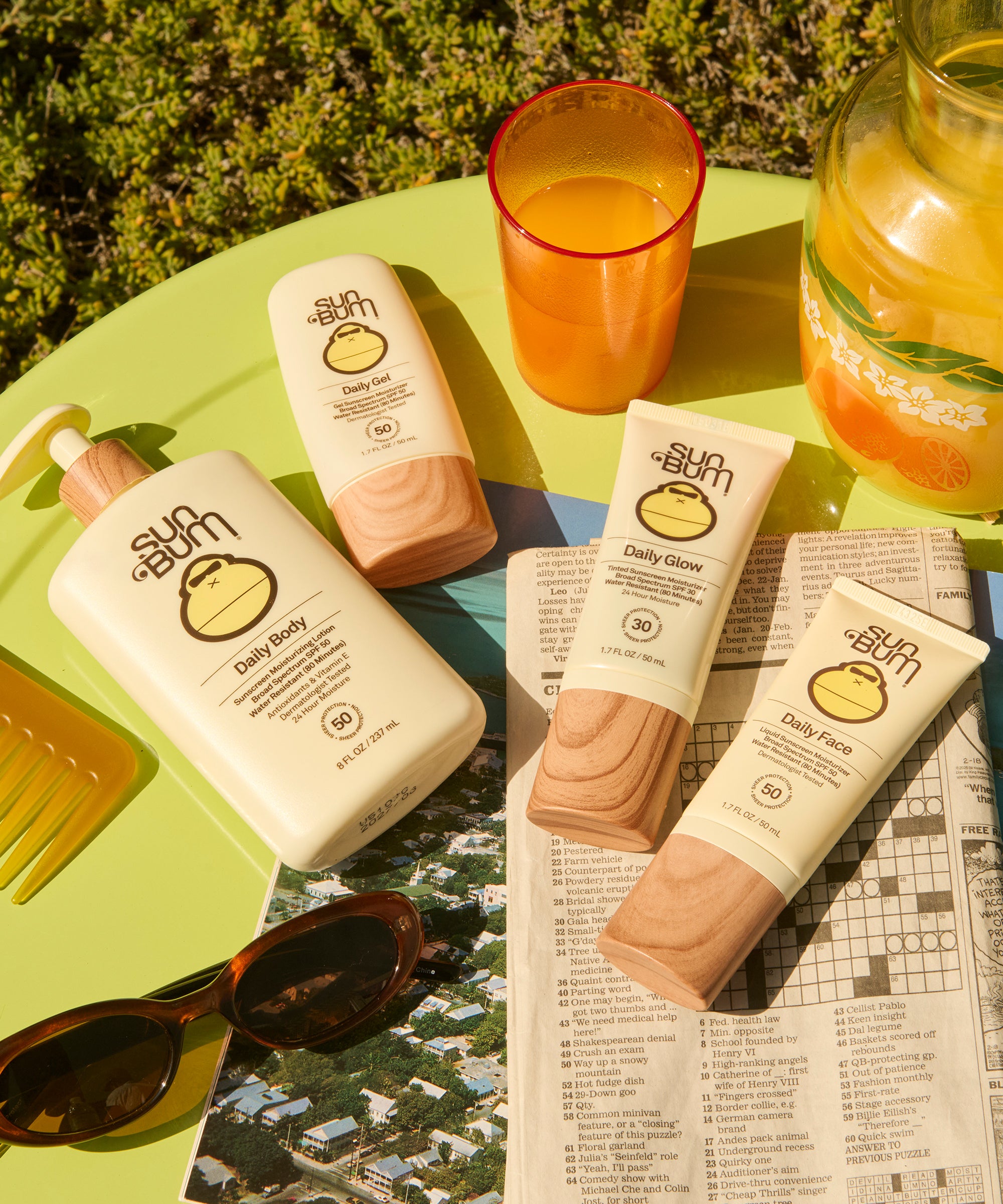 Sunscreen products and a glass of orange juice on a table with a newspaper underneath.
