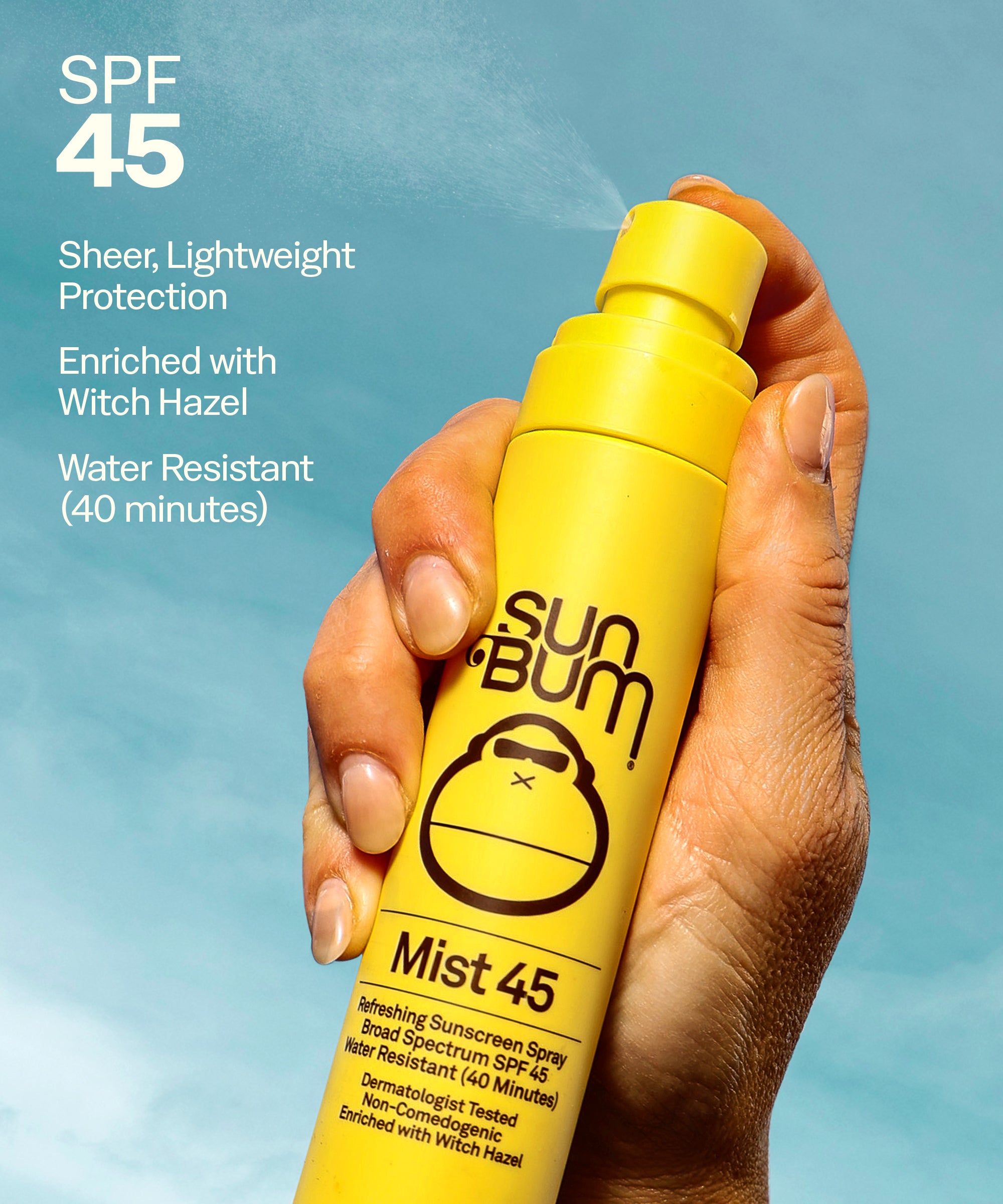 Hand holding Sun Bum SPF 15 Tanning Oil + Mist 45 yellow spray bottle misting sunscreen against sky background