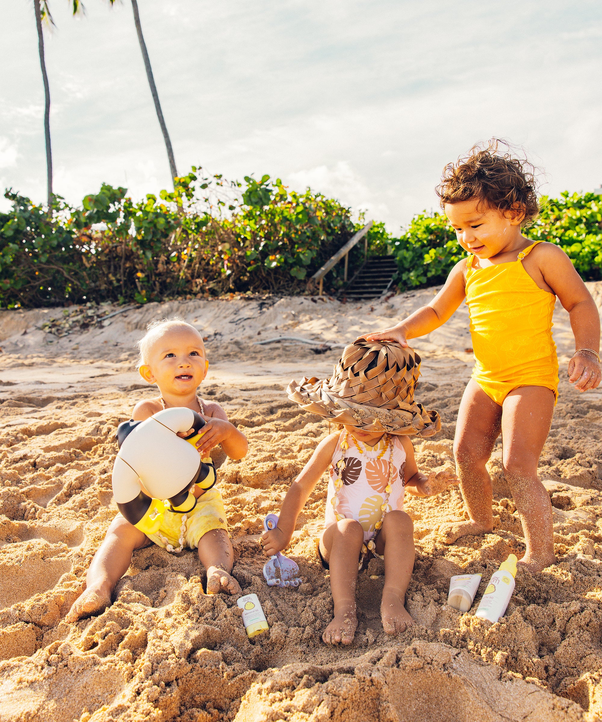 Three toddlers playing on the beach with Baby Bum Mineral SPF 50 Sunscreen Spray for sun protection, Baby Bum.