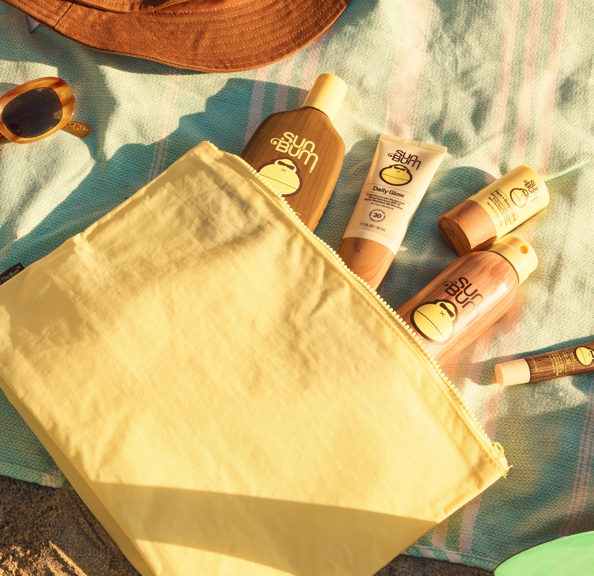 Sunscreen bottles and a yellow bag on a towel with sunglasses