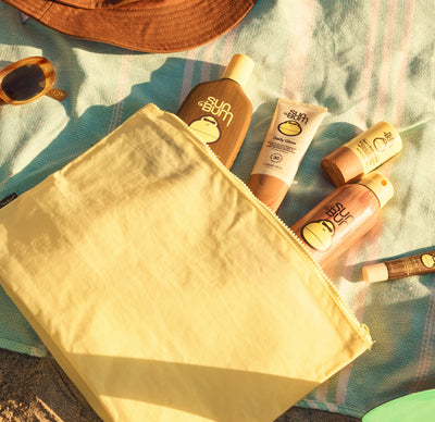 Sunscreen bottles and a yellow bag on a towel with sunglasses
