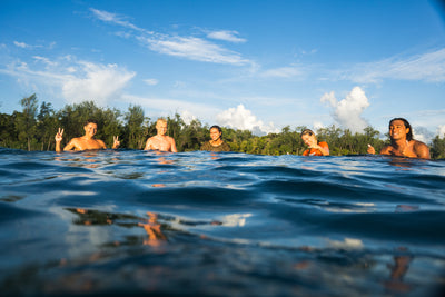 People in the water with a scenic background of trees and blue sky.