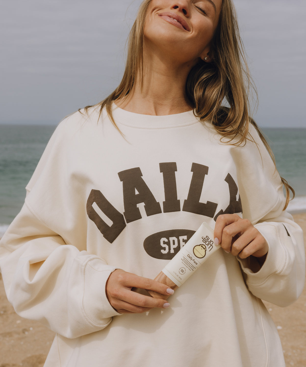 Woman wearing a white sweatshirt with 'DAILY' text on a beach