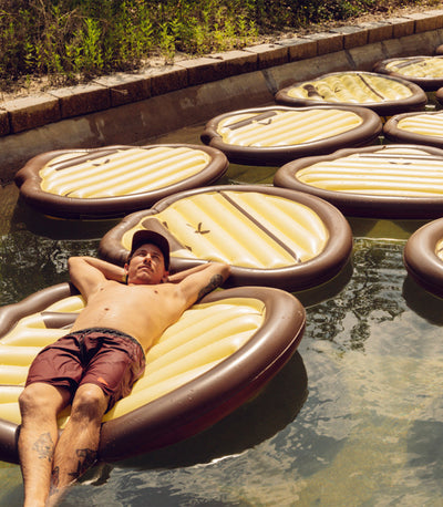 Man lying on a floating inflatable lounger in a pool with multiple similar loungers around.