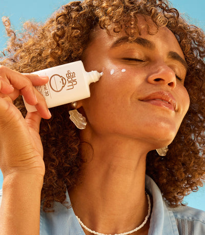 Woman applying sunscreen to her face with a tube labeled 'YKPR' against a clear blue sky.