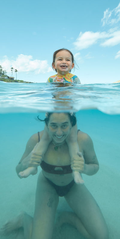 Woman swimming in the ocean with a baby on her shoulders
