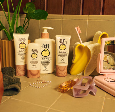 Sun Bum sunscreen products on a bathroom counter with a plant and towel in the background.
