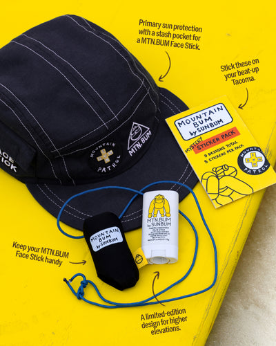 Navy cap with branding, MTN BUM face stick, and sticker pack on a yellow background