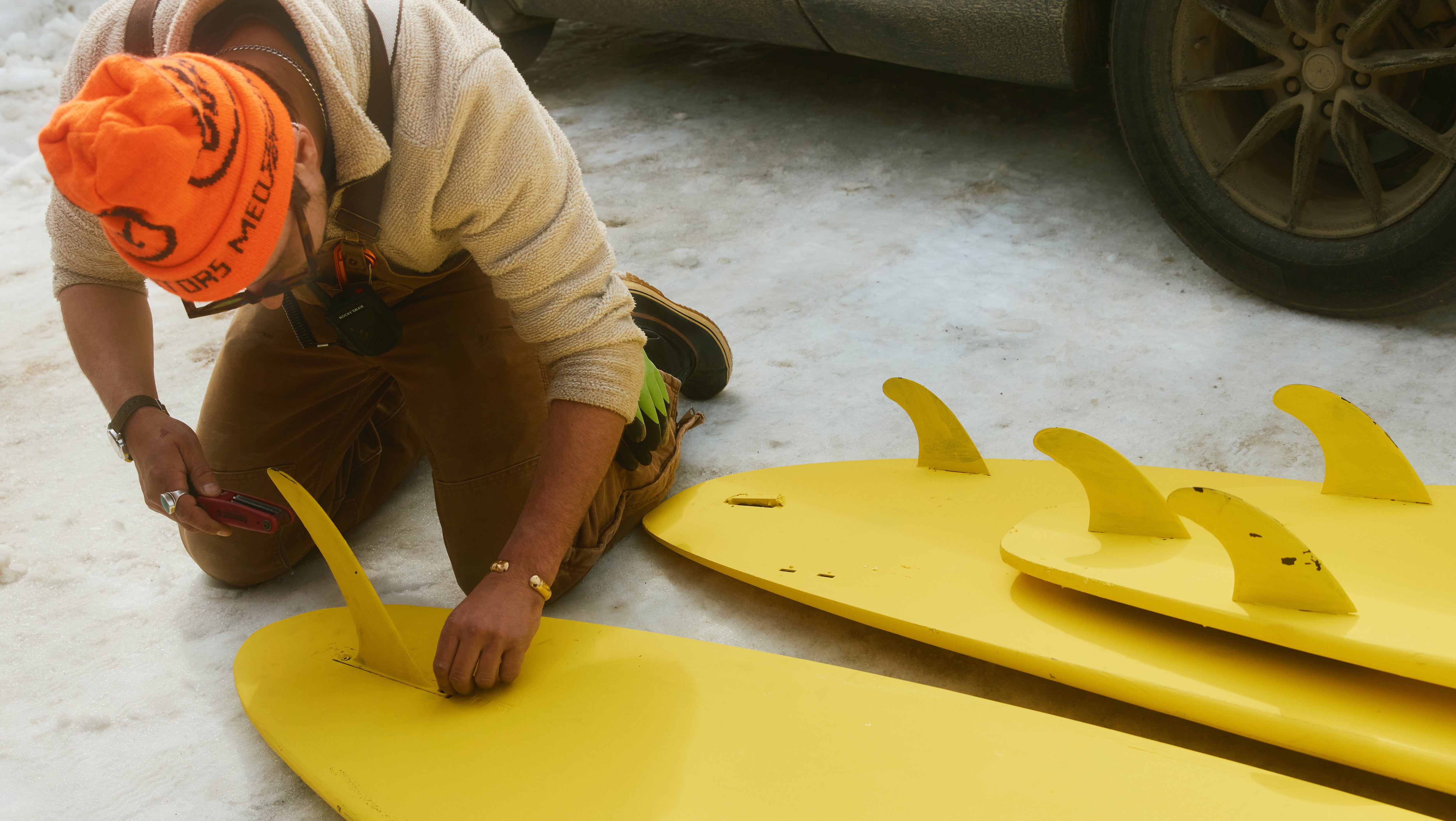 Person working on a yellow surfboard with fins in an indoor setting
