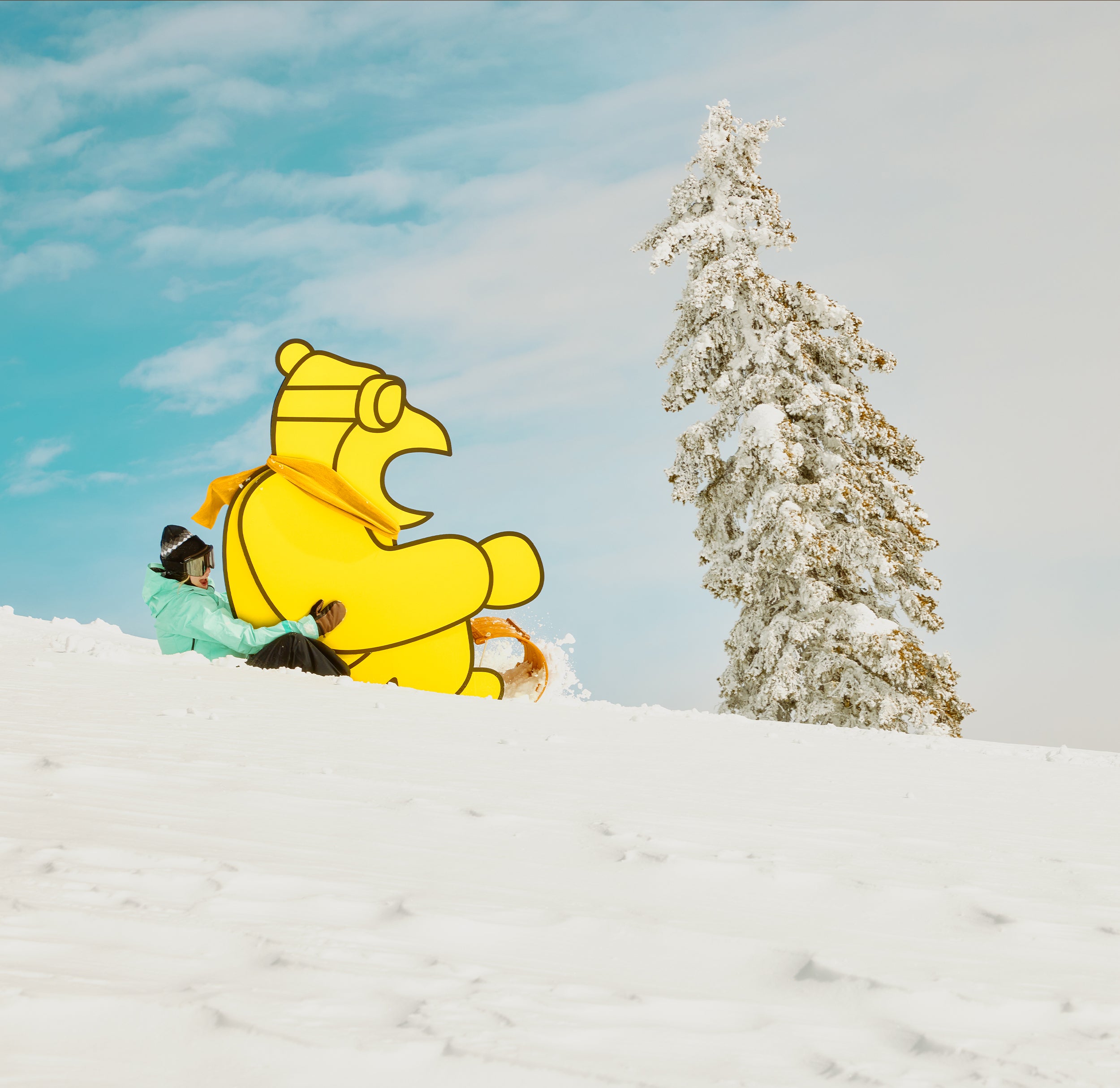 Person holding a large inflatable yellow duck in a snowy landscape with a tree.