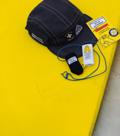 Black cap and stickers on a yellow surface with 'Mountain Bum' branding.
