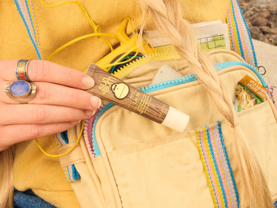Hand holding a wooden tool with a yellow jacket and colorful bag in the background
