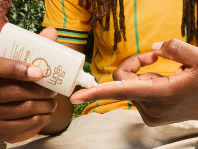 Person applying lotion from a bottle labeled 'Sun Bum' to their hand.